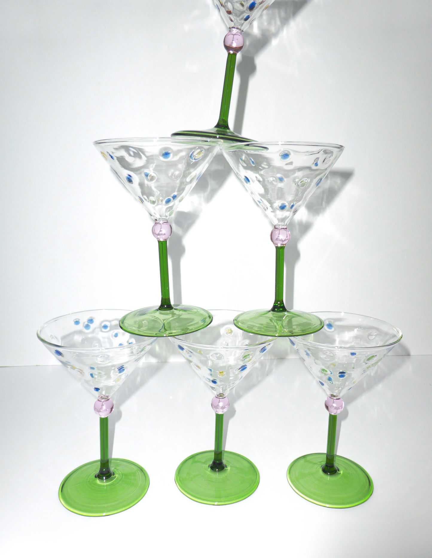 Image of a tower of funky and unique martini glasses with green stem and pink ball stem detailing with polka dot glass 