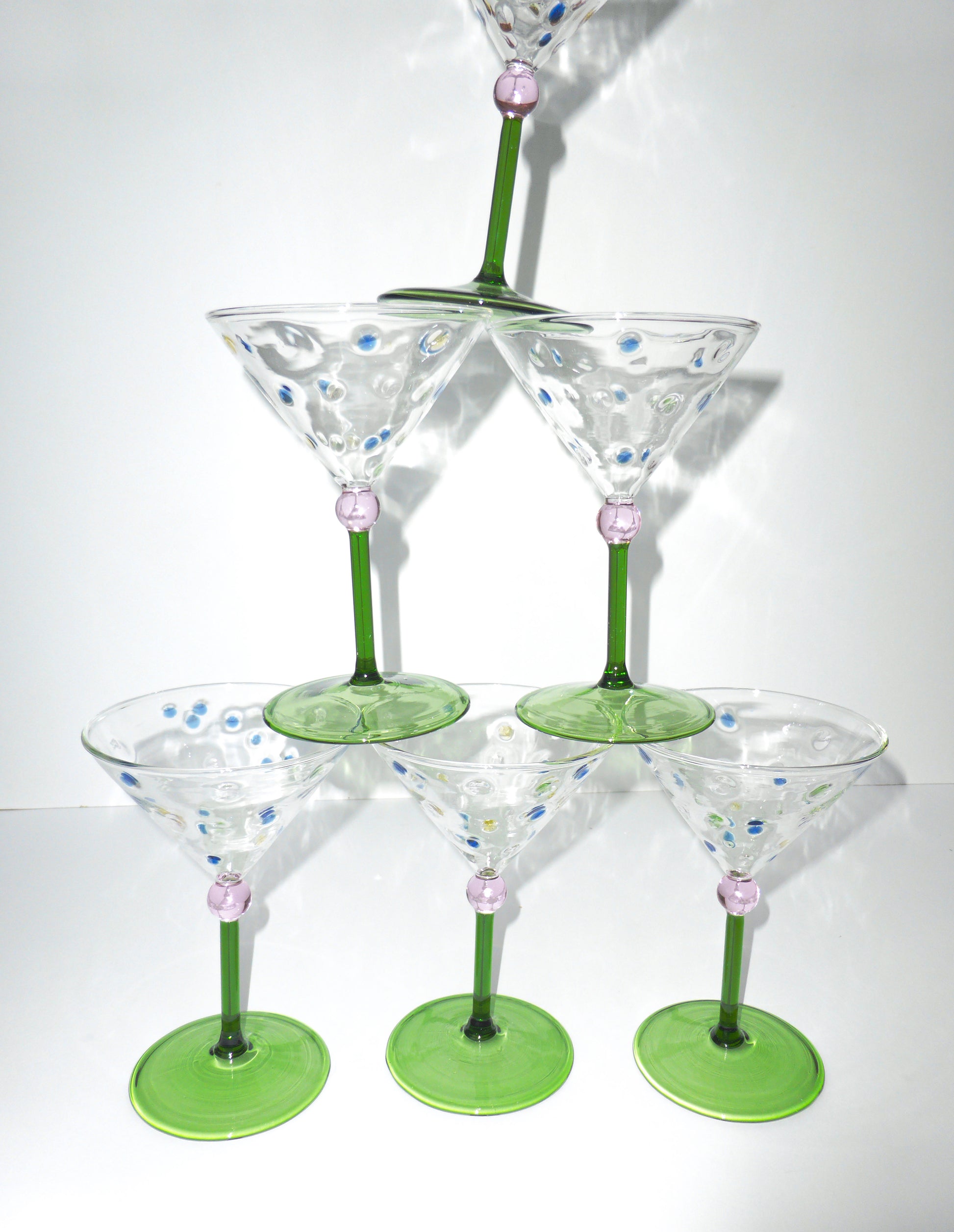 Image of a tower of funky and unique martini glasses with green stem and pink ball stem detailing with polka dot glass 